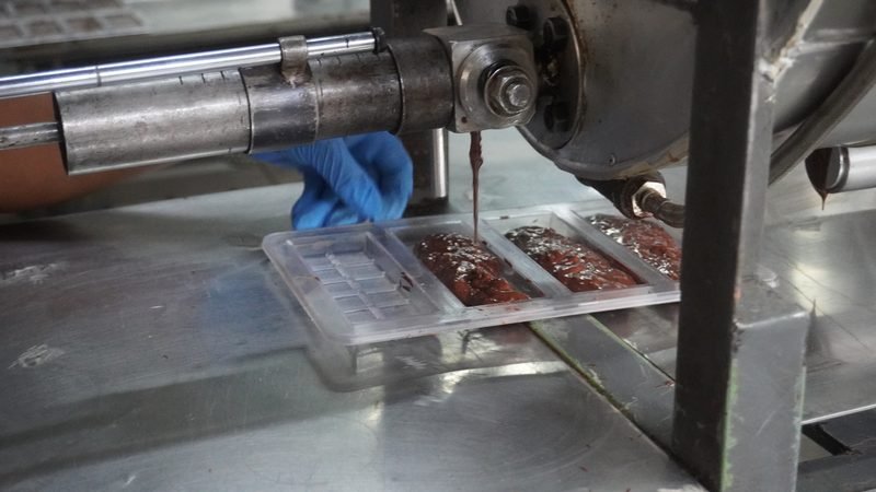 Manos con guantes llenando moldes de barras de chocolate en la planta